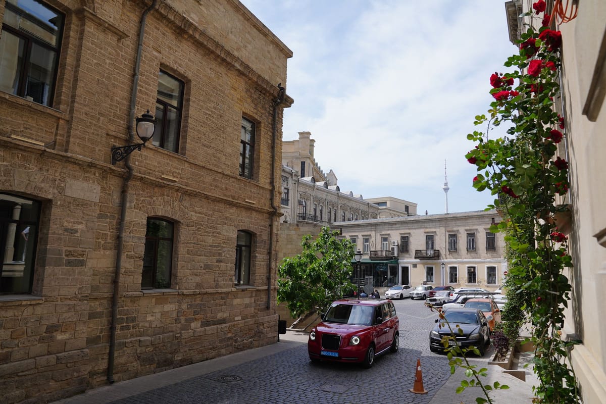 Červený taxík v ulici z pieskovcových domov v Baku s televíznou vežou v pozadí