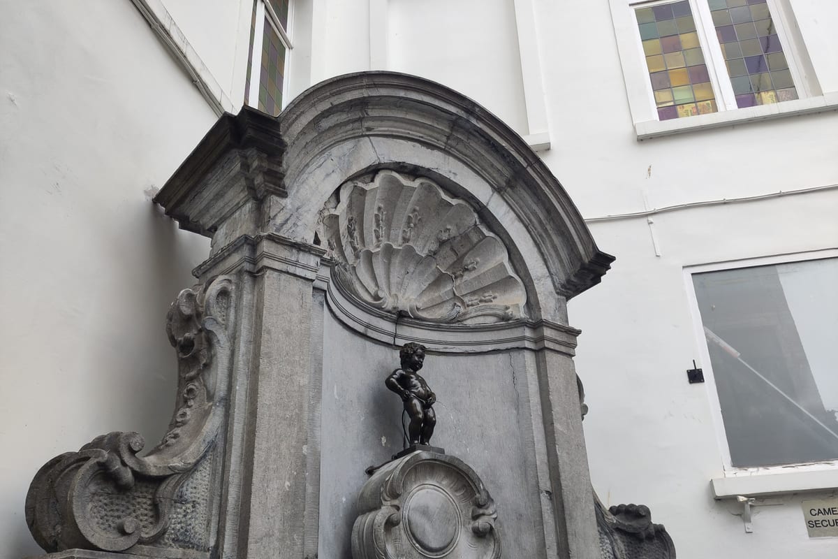 Bronzová soška Manneken Pis v kamennom výklenku na rohu ulice v Bruseli