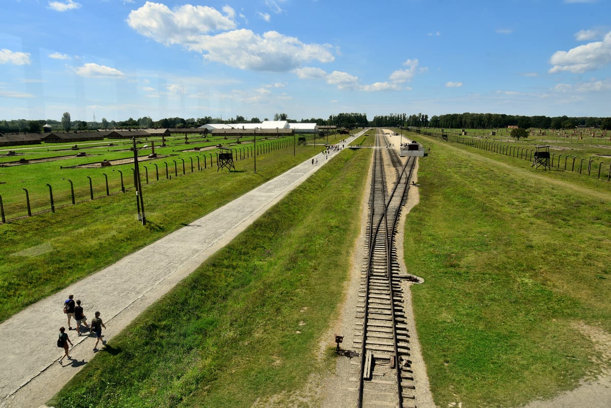 Koľajnice vedúce do tábora Auschwitz II-Birkenau a rady drevených barakov za plotom