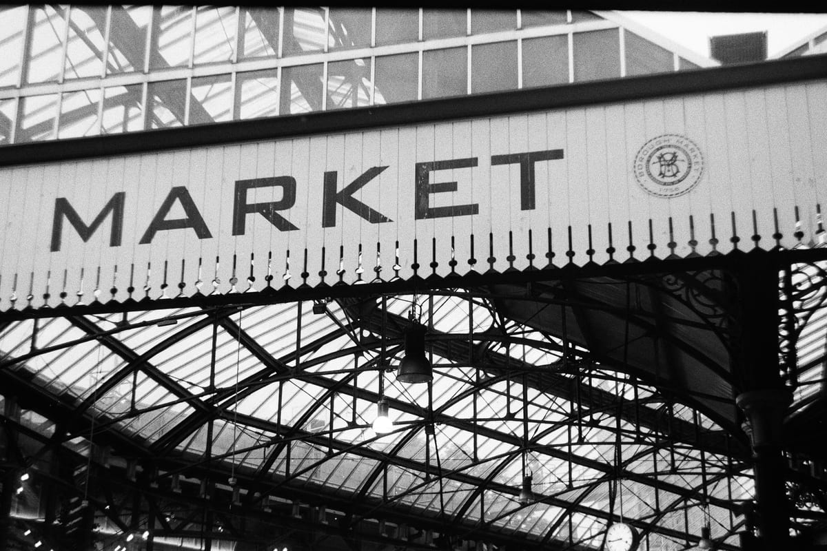 Čiernobiela fotka nápisu Market a železnej strechy trhu Borough Market
