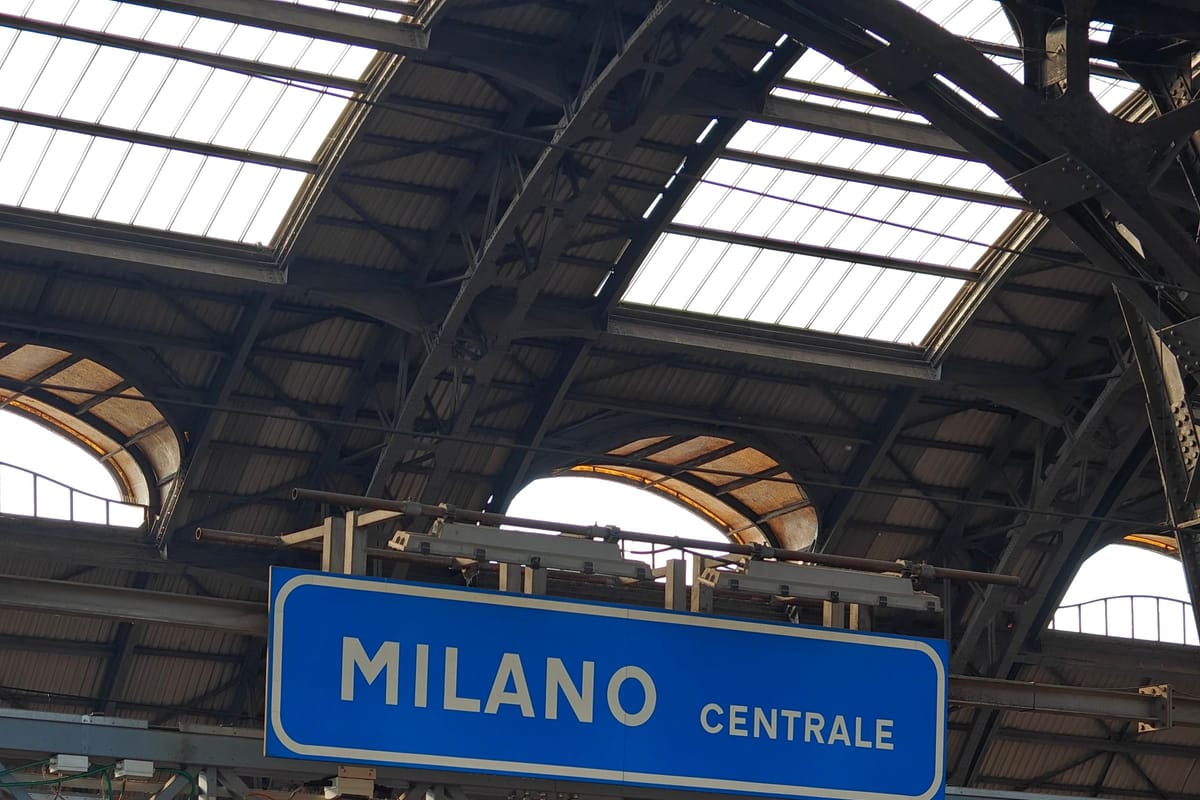 Modrá tabuľa Milano Centrale nad nástupišťom pod oceľovou strechou stanice