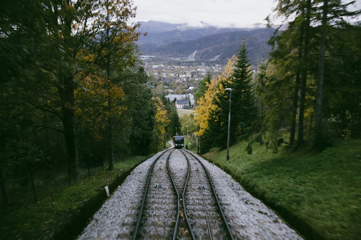 Trať pozemnej lanovky v jesennom lese, v pozadí strechy Zakopaného