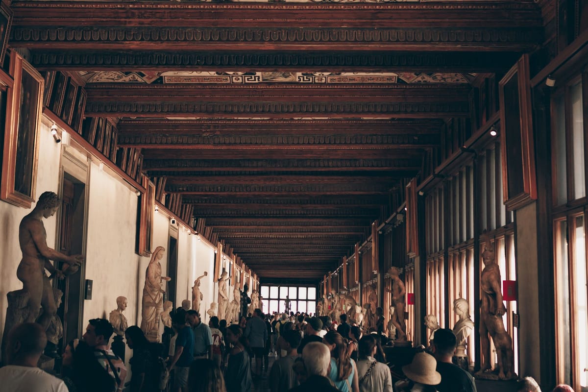 Návštevníci v dlhej chodbe Galérie Uffizi s maľovaným stropom a antickými sochami