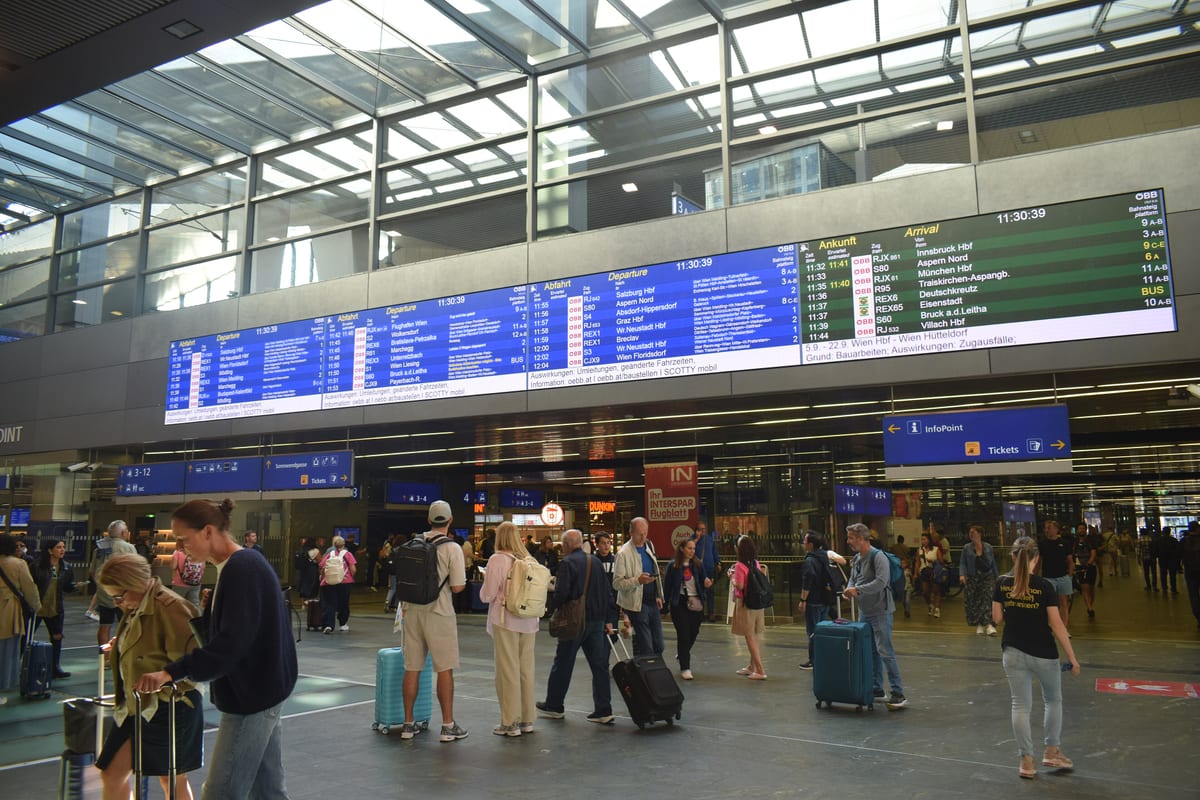 Hala stanice Wien Hauptbahnhof s tabuľami odchodov a cestujúcimi s kuframi