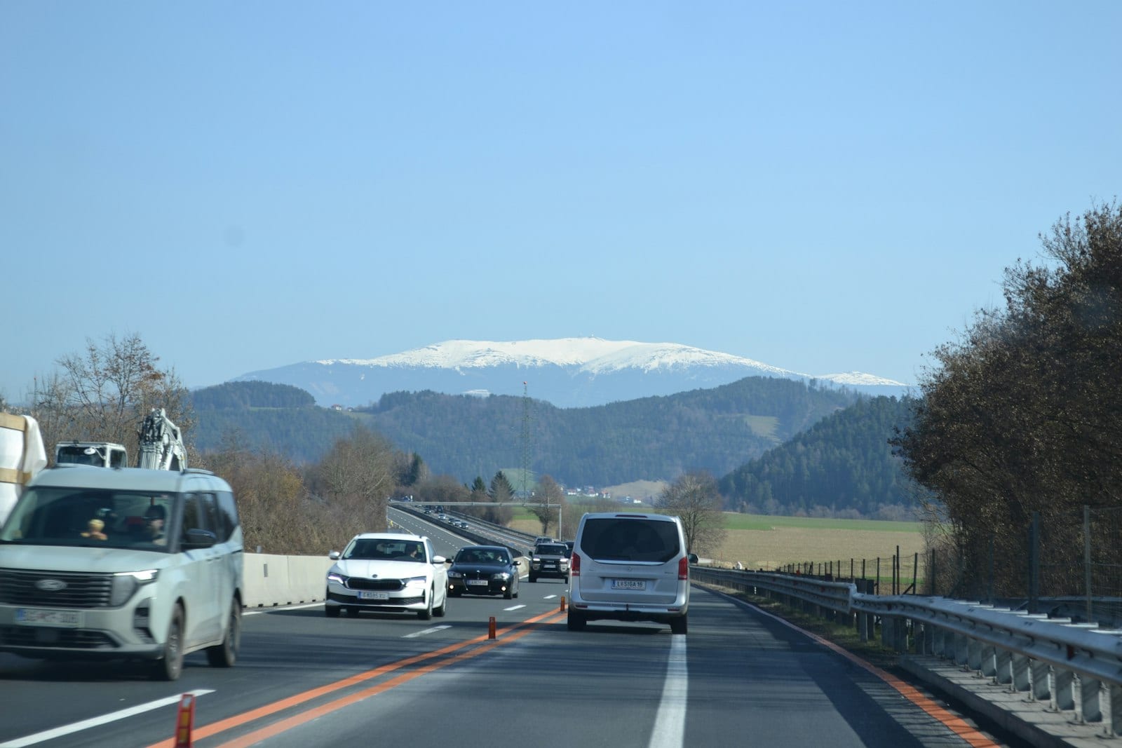 Autá na diaľnici v zúženom úseku, v pozadí zalesnené kopce a zasnežený hrebeň