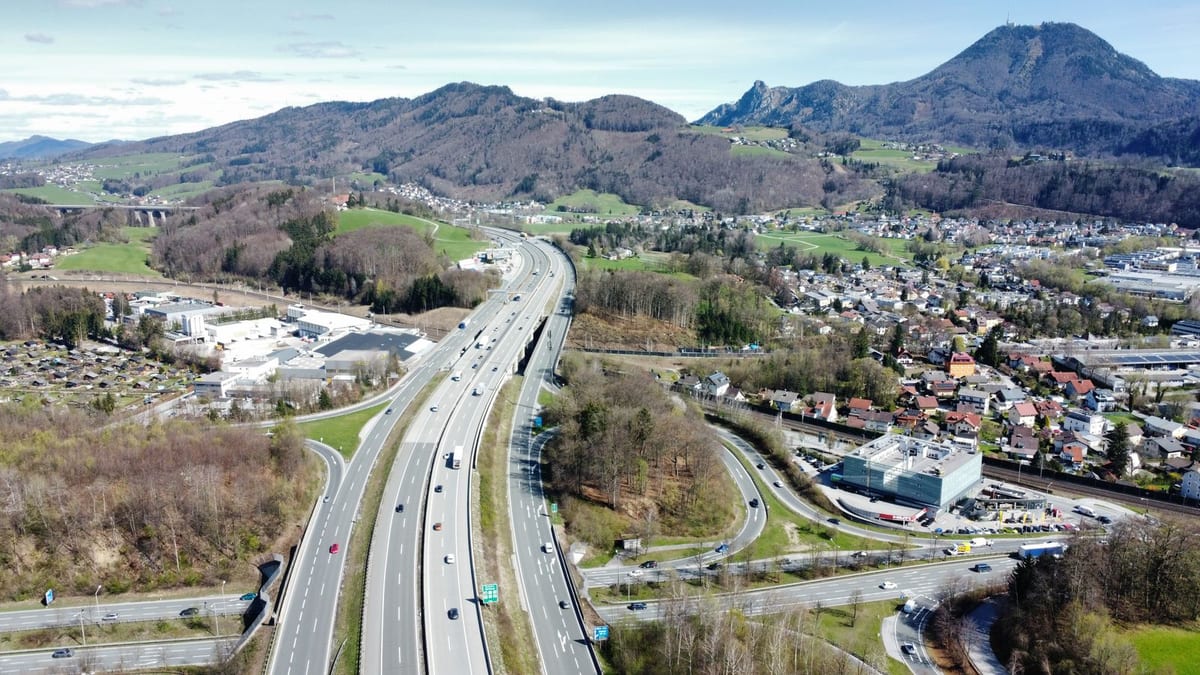 Diaľnica s výjazdmi pri Salzburgu z vtáčej perspektívy, okolo domy a zalesnené vrchy