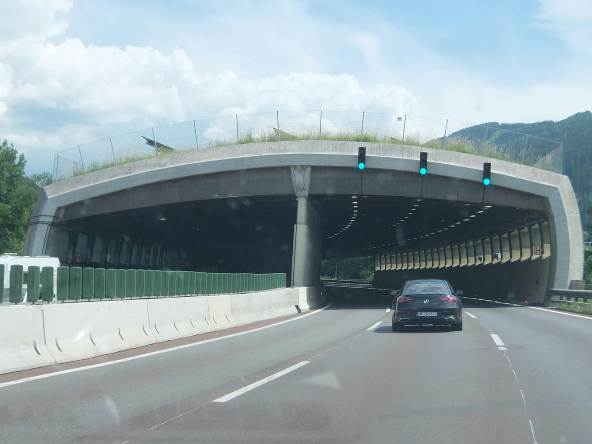 Auto vchádza do portálu diaľničného tunela, nad pruhmi svietia zelené semafory