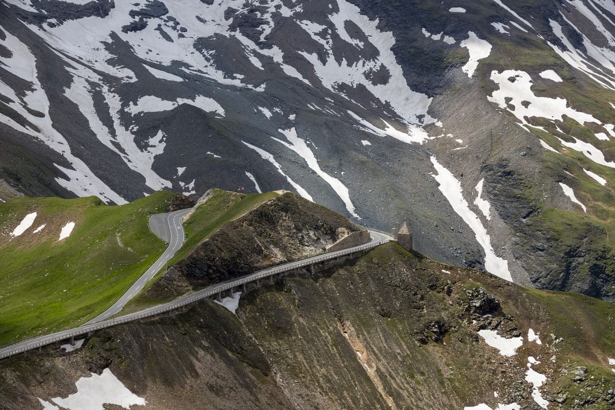 Serpentíny cesty Großglockner Hochalpenstraße medzi zelenými svahmi a snehovými poľami