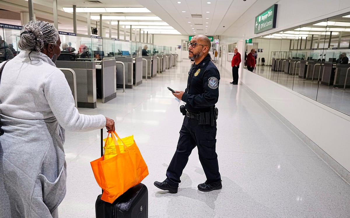 Úradník CBP s mobilom v príletovej hale letiska v Baltimore a cestujúca s kufrom a oranžovou taškou