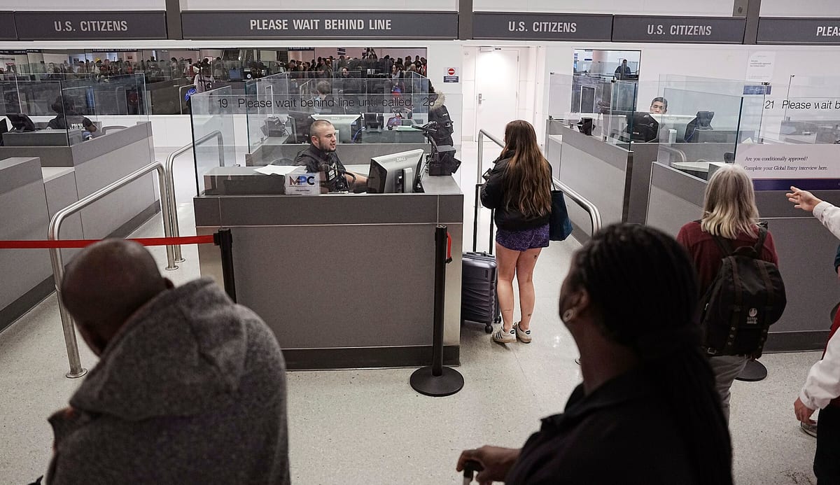 Kabínky pasovej kontroly CBP s nápisom Please wait behind line, úradník za sklom a cestujúci čakajúci za čiarou
