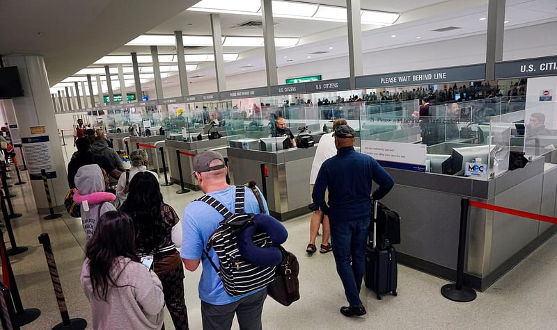 Cestujúci čakajú v rade na pasovú kontrolu CBP na letisku v Baltimore, nad kabínkami nápis Please wait behind line a vpravo značka MPC