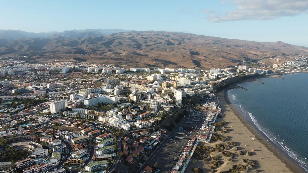 Letecký pohľad na Playa del Inglés a Maspalomas s hotelmi, dlhou plážou a holými horami v pozadí.