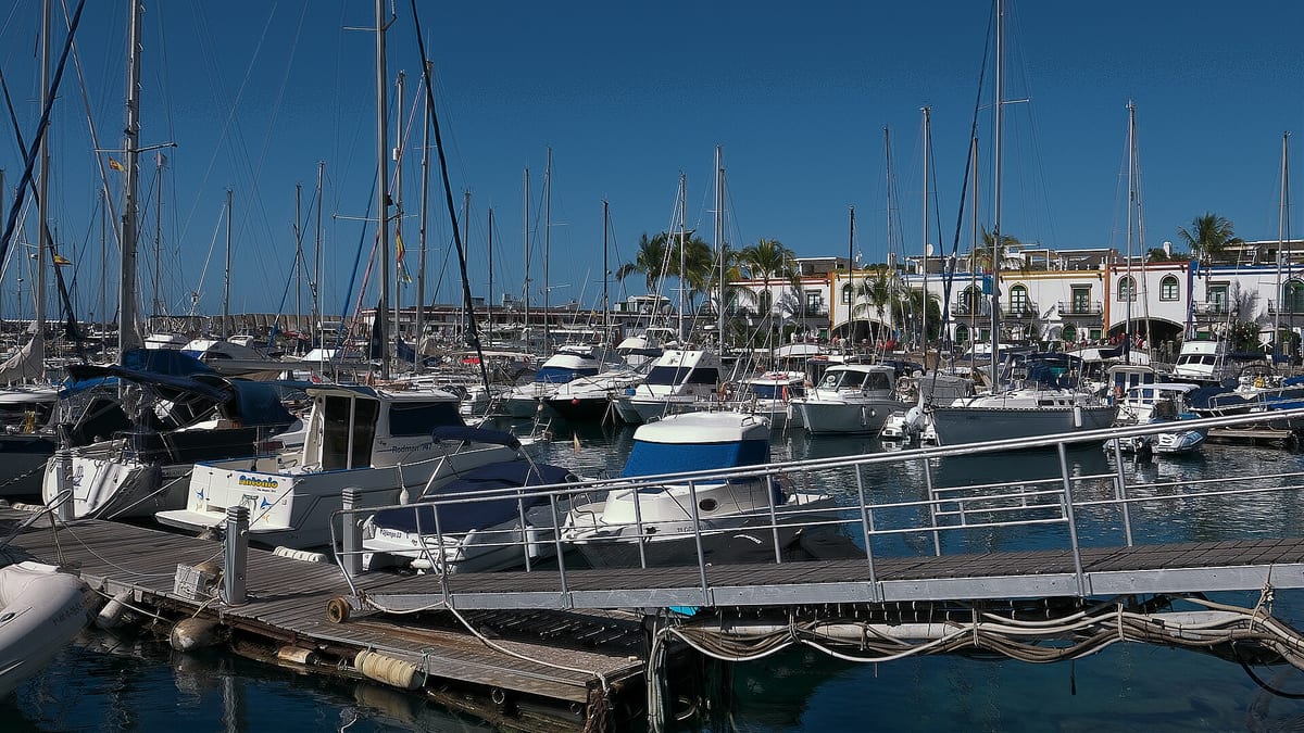 Jachty a plachetnice v prístave Puerto de Mogán s bielymi domami a palmami v pozadí.