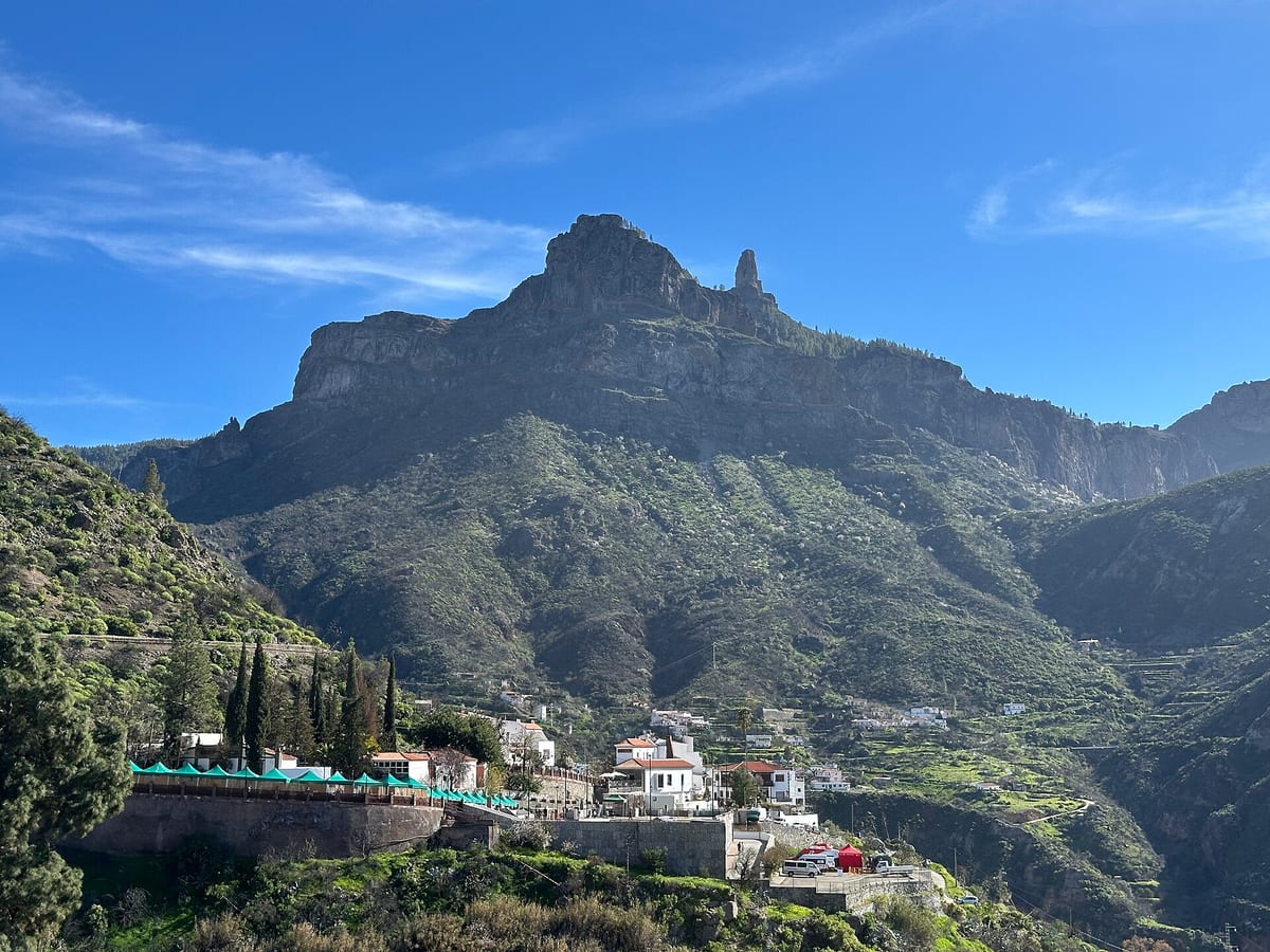 Skala Roque Nublo na hrebeni nad dedinou Tejeda so zelenými svahmi a domami v údolí.