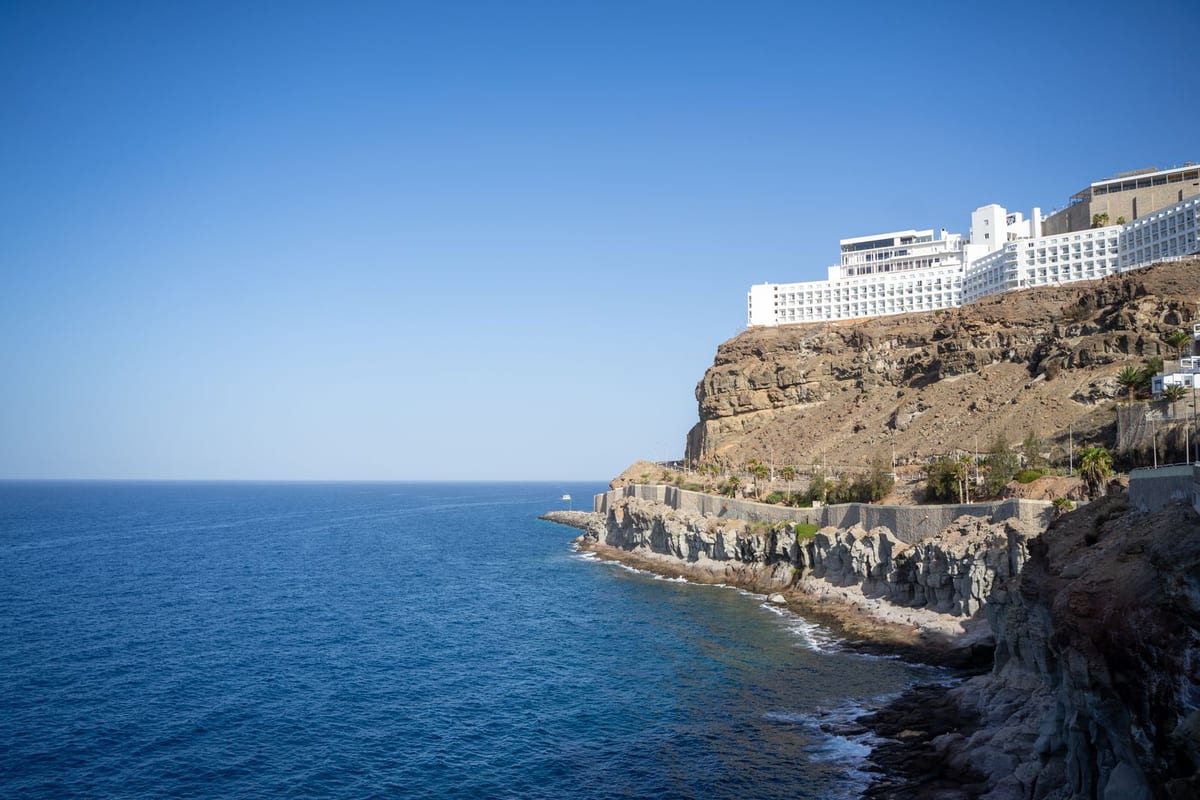 Skalnaté útesy v Puerto Rico na juhozápade Gran Canarie s bielym hotelom nad modrým oceánom.