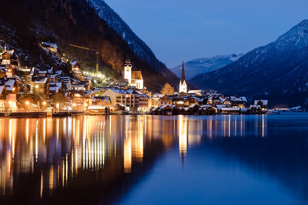 Osvetlený Hallstatt sa po zotmení odráža v tichom jazere, nad ním zasnežené svahy