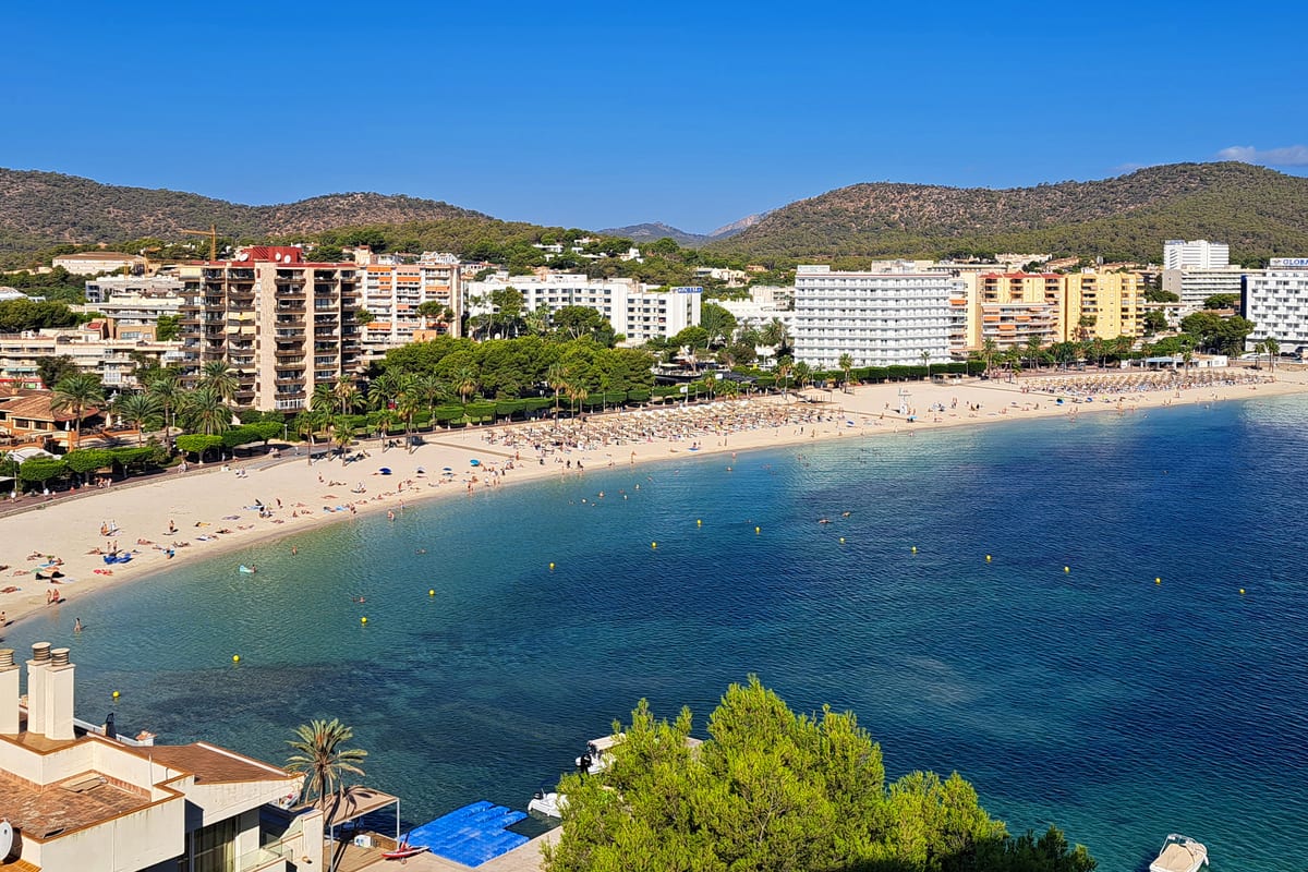 Piesočná pláž v zátoke Palmanova na Mallorke s hotelmi a kopcami