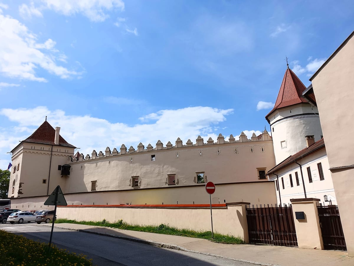 Hradby Kežmarského hradu a autá zaparkované pri ceste pred nimi