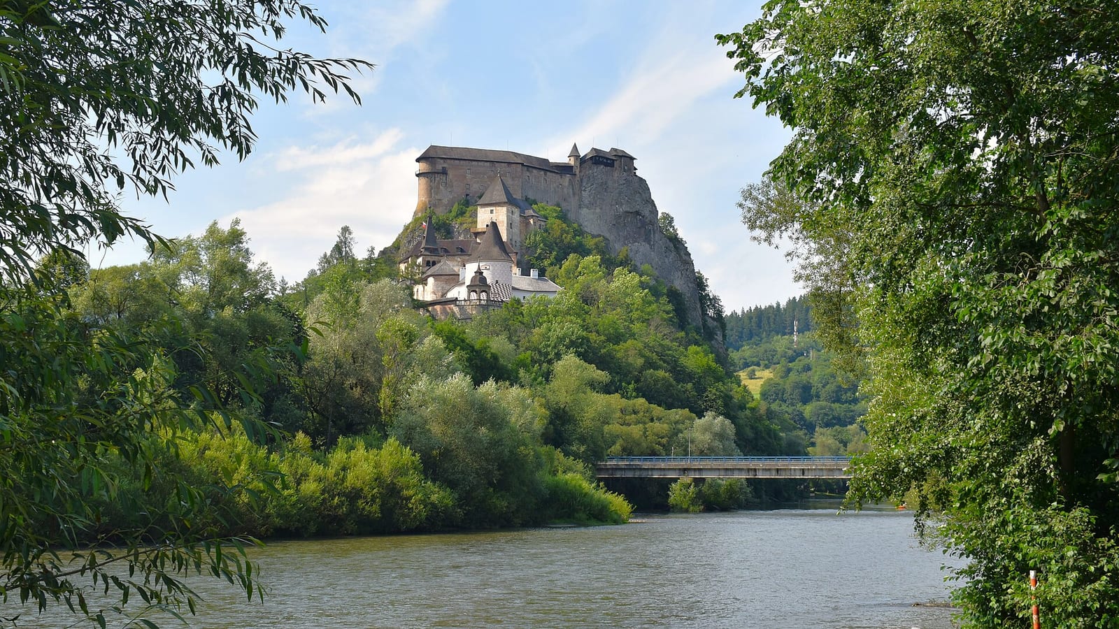 Oravský hrad na skale nad riekou Orava, v popredí stromy na brehu
