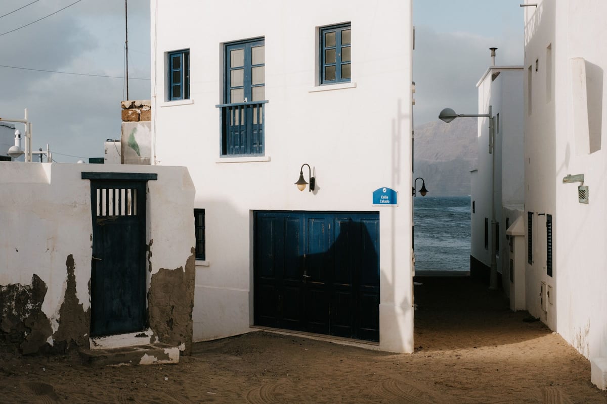 Biele domy s modrými dverami na pieskovej uličke v Caleta de Famara