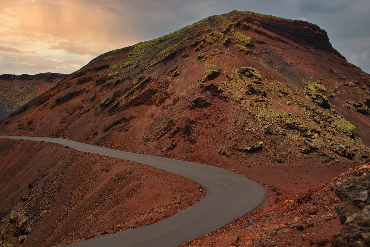 Úzka cesta, ktorá sa kľukatí po červenom sopečnom svahu na Lanzarote
