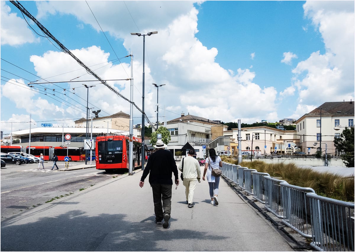 Ľudia kráčajú k budove Bratislava hlavná stanica, vpravo stoja červené trolejbusy