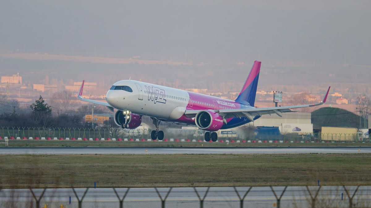 Lietadlo Wizz Air pri vzlete z dráhy, za ním domy mesta v opare