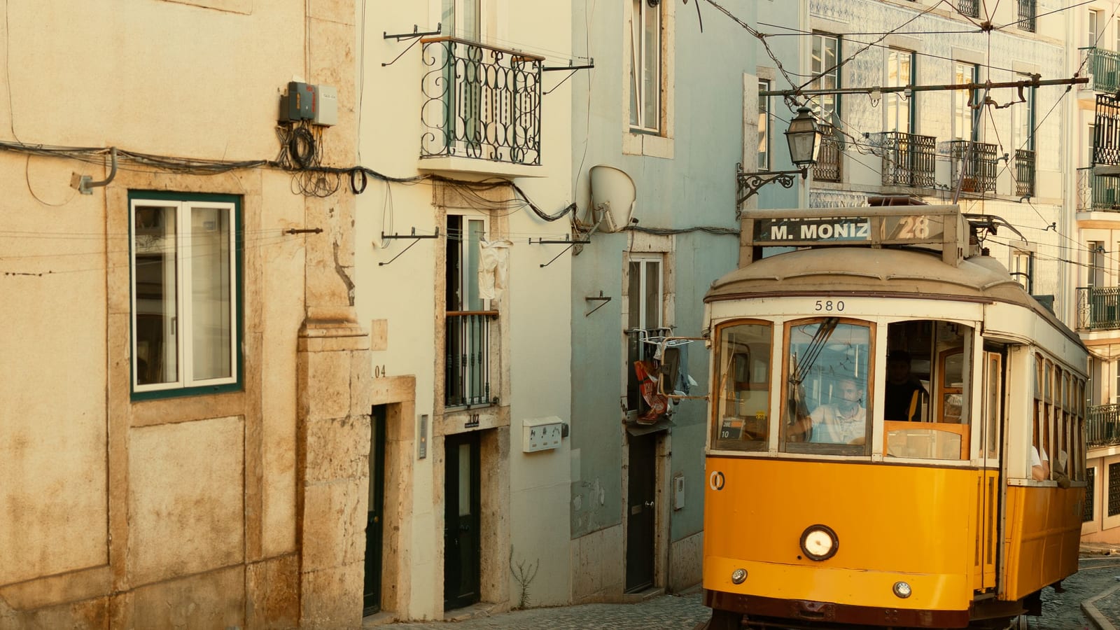 Žltá električka linky 28 s tabuľou Martim Moniz v úzkej ulici Lisabonu