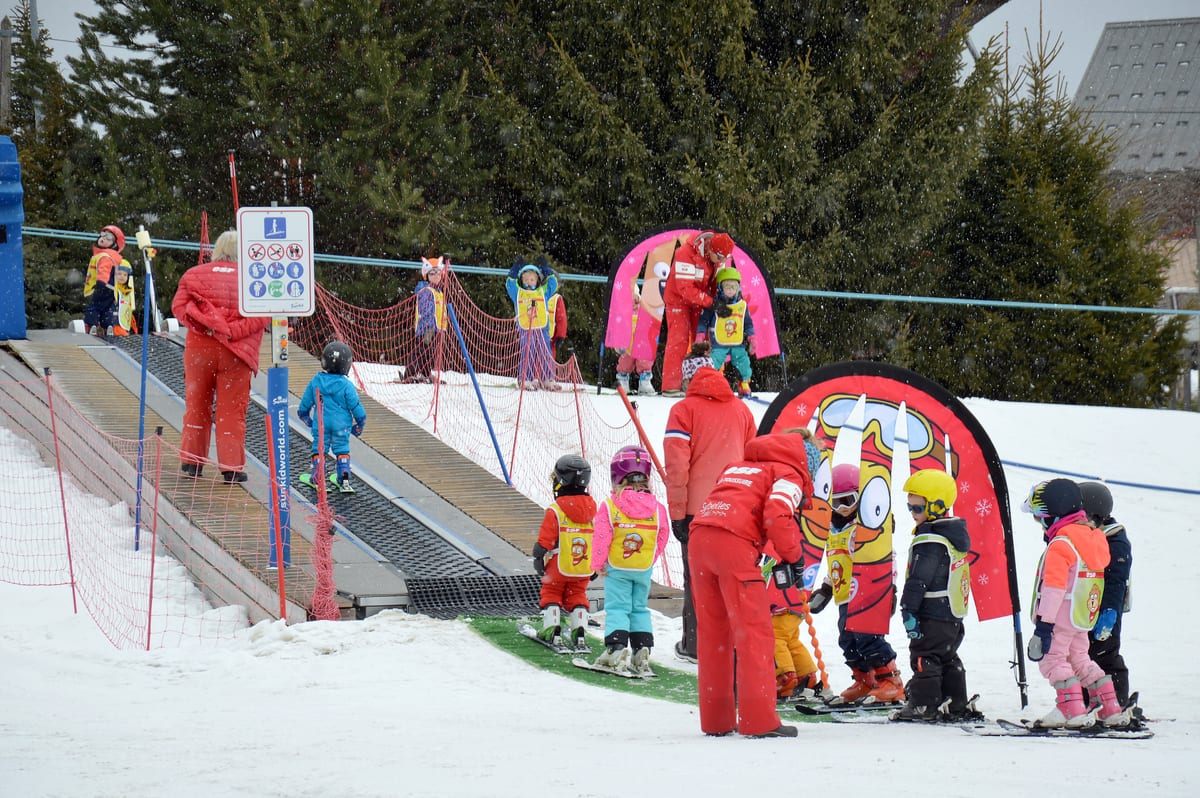Deti s prilbami a reflexnými vestami v lyžiarskej škole pri pohyblivom páse