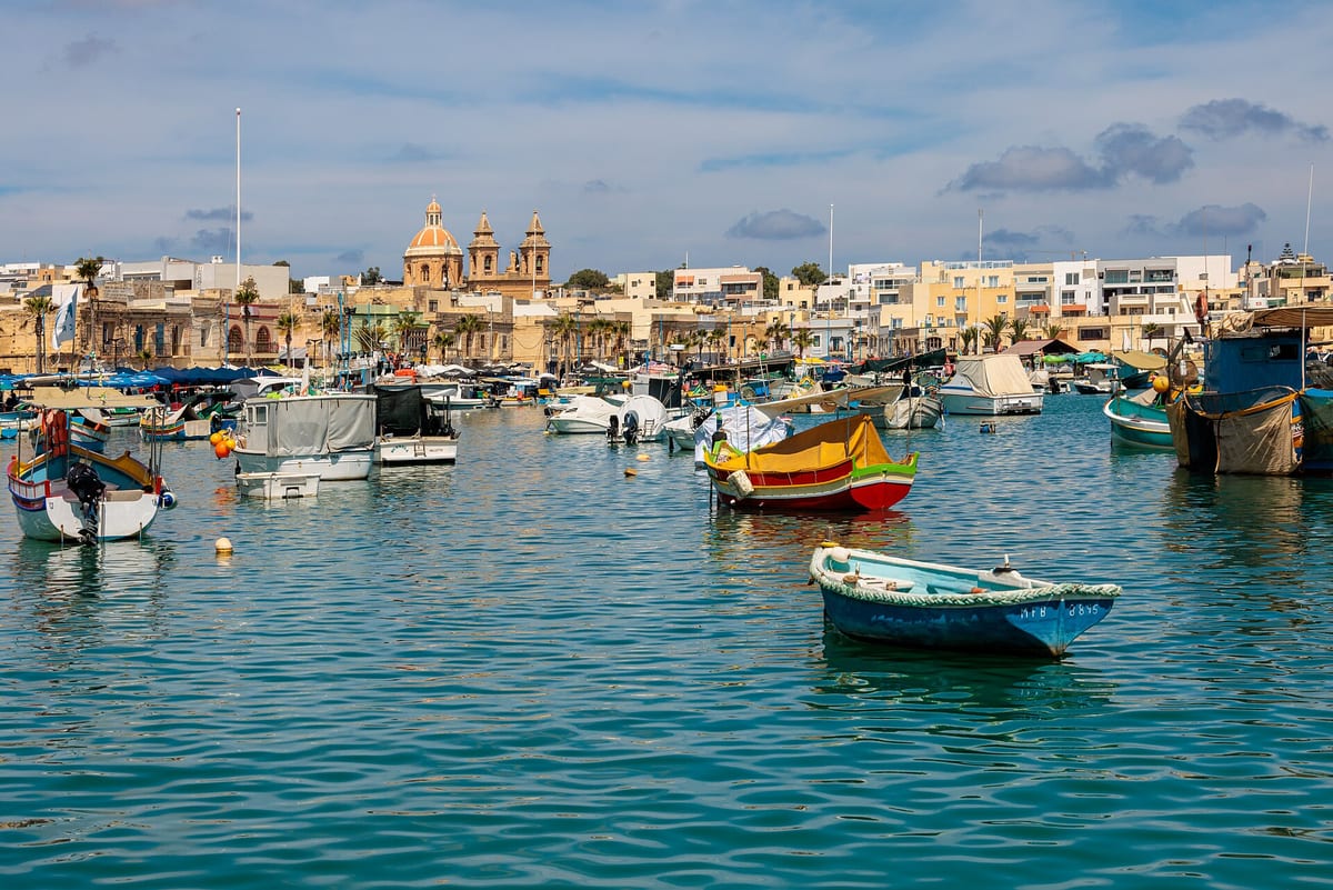 Pestré rybárske loďky luzzu v zálive Marsaxlokk pred kostolom na nábreží