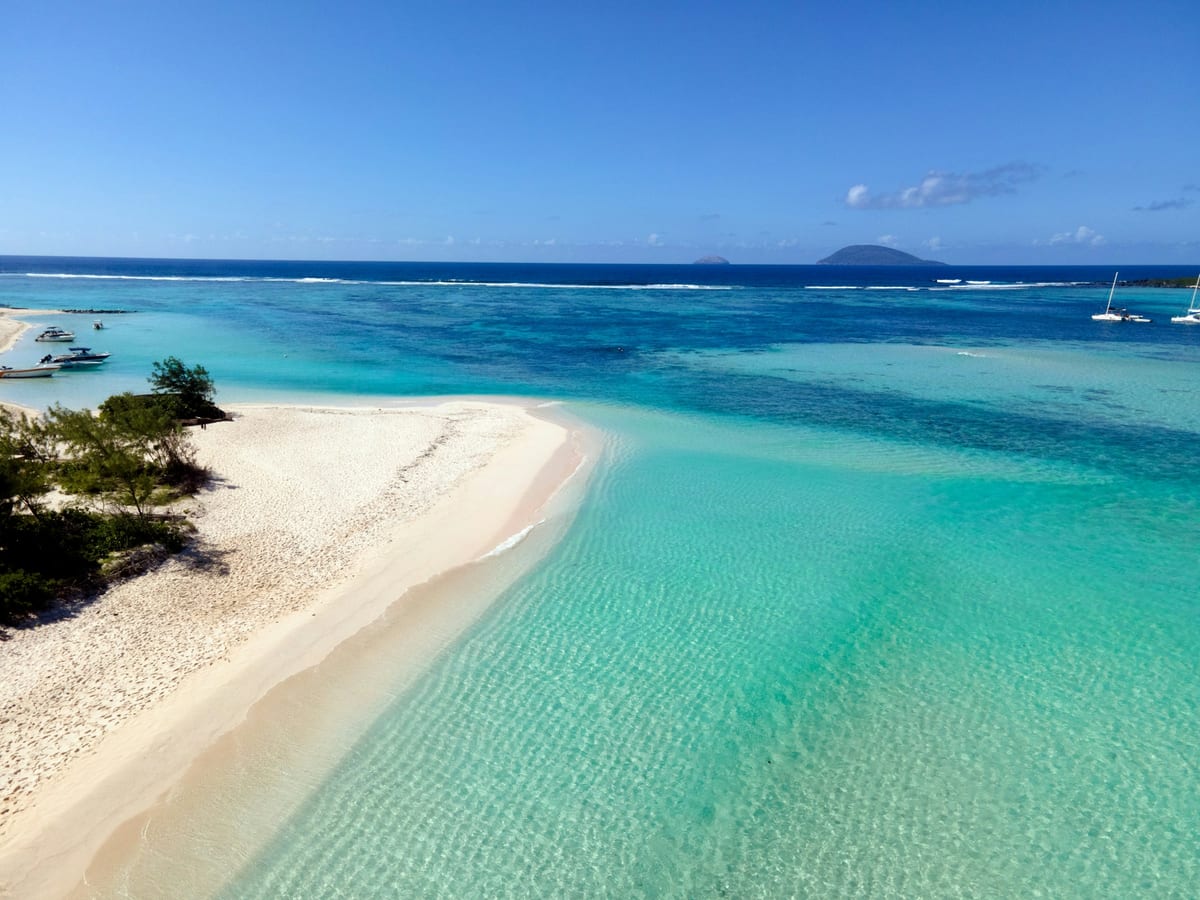 Biela piesočná kosa, tyrkysová lagúna a ukotvené lode pri ostrovčeku Flat Island na severe Maurícia
