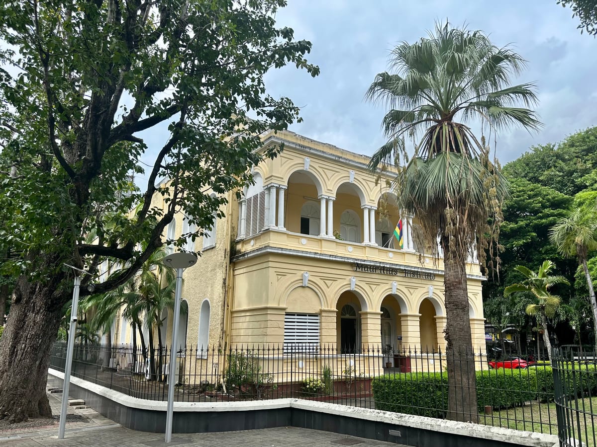 Žltá koloniálna budova prírodovedného múzea v Port Louis s arkádami a palmou pred vchodom