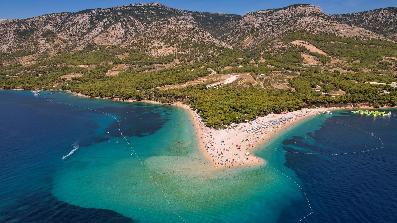 Pláž Zlatni rat v Bole na ostrove Brač zo vzduchu, za ňou svahy pohoria Vidova gora.