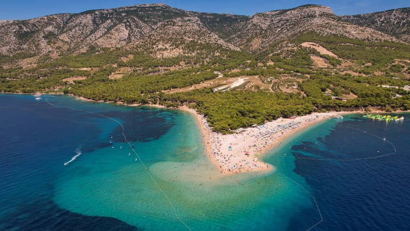 Pláž Zlatni rat v Bole na ostrove Brač zo vzduchu, za ňou svahy pohoria Vidova gora.