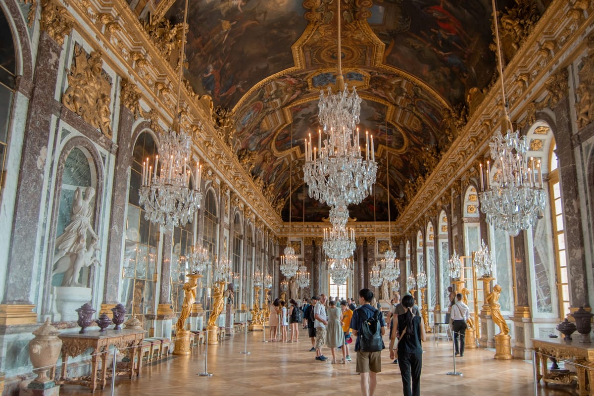 Návštevníci v Zrkadlovej sieni zámku Versailles s lustrami