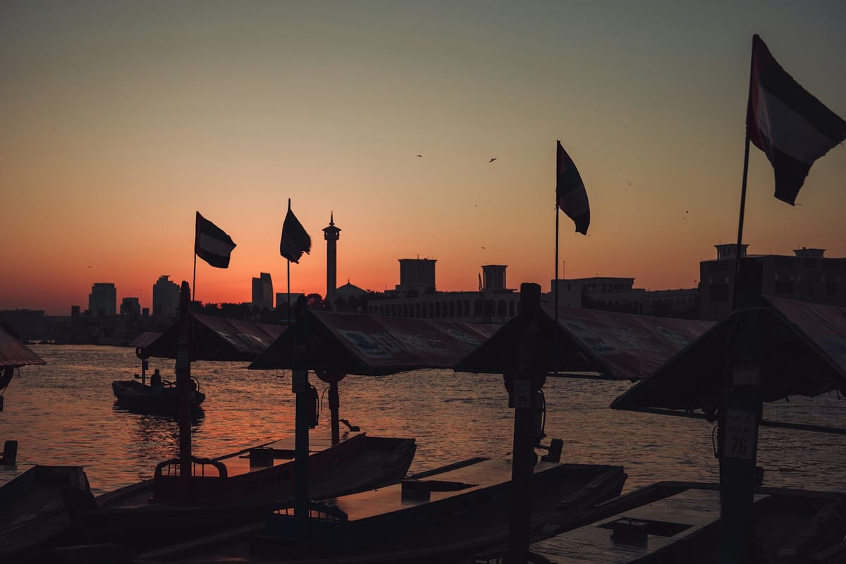 Drevené loďky abra pri móle na zálive Dubai Creek pri západe slnka, vlajky SAE