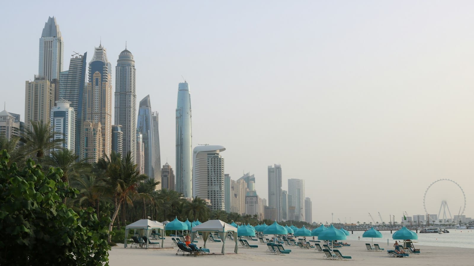 Pláž s ležadlami a slnečníkmi pod mrakodrapmi Dubai Marina v letnom opare