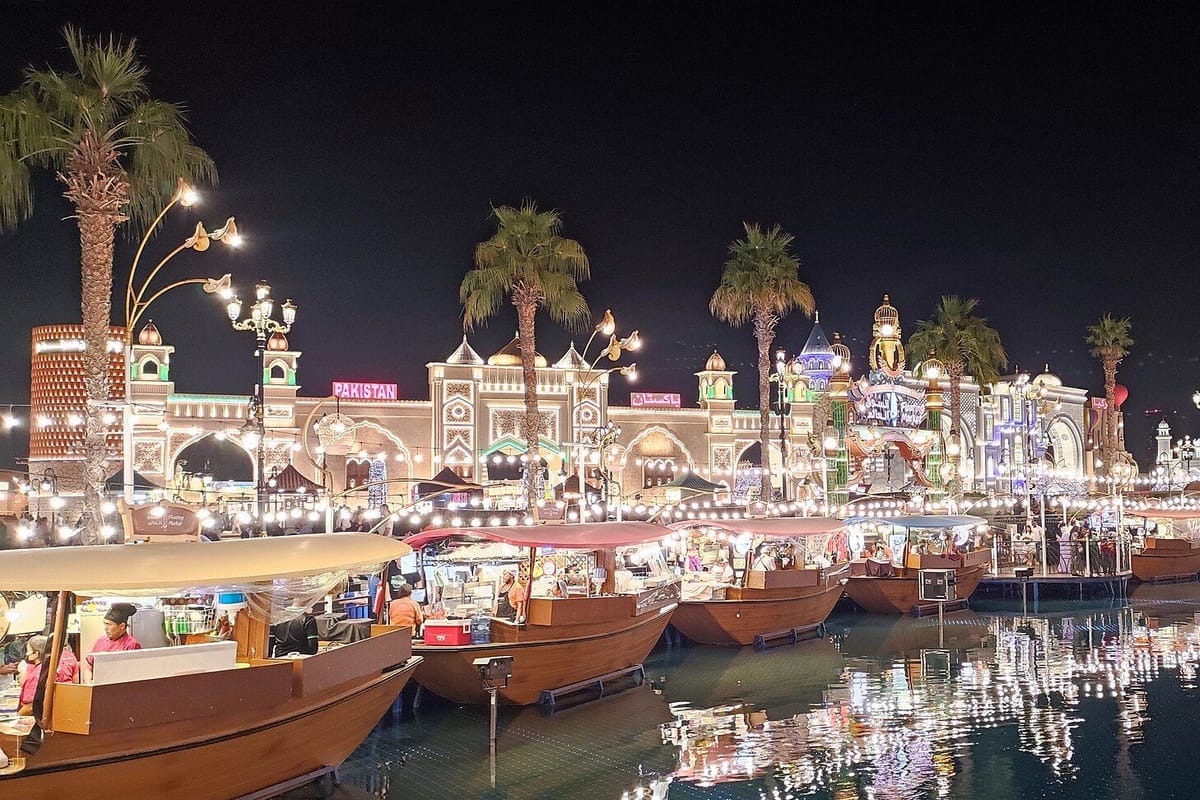 Osvetlené pavilóny a drevené lodičky na kanáli v Global Village v Dubaji večer
