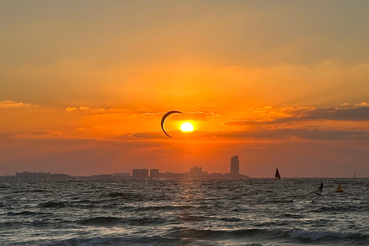 Kitesurfer na Kite Beach v Dubaji pri západe slnka, na obzore silueta hotela Burdž al-Arab
