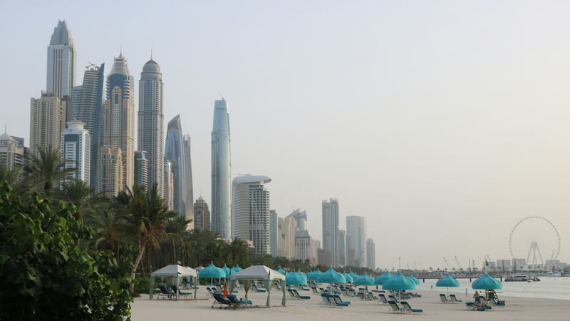Pláž s ležadlami a slnečníkmi pod mrakodrapmi Dubai Marina v letnom opare