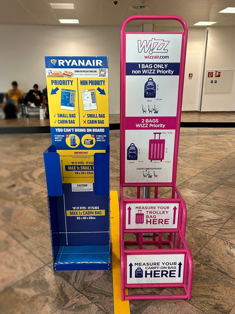 Modré meradlo príručnej batožiny Ryanair vedľa ružového meradla Wizz Air v odletovej hale