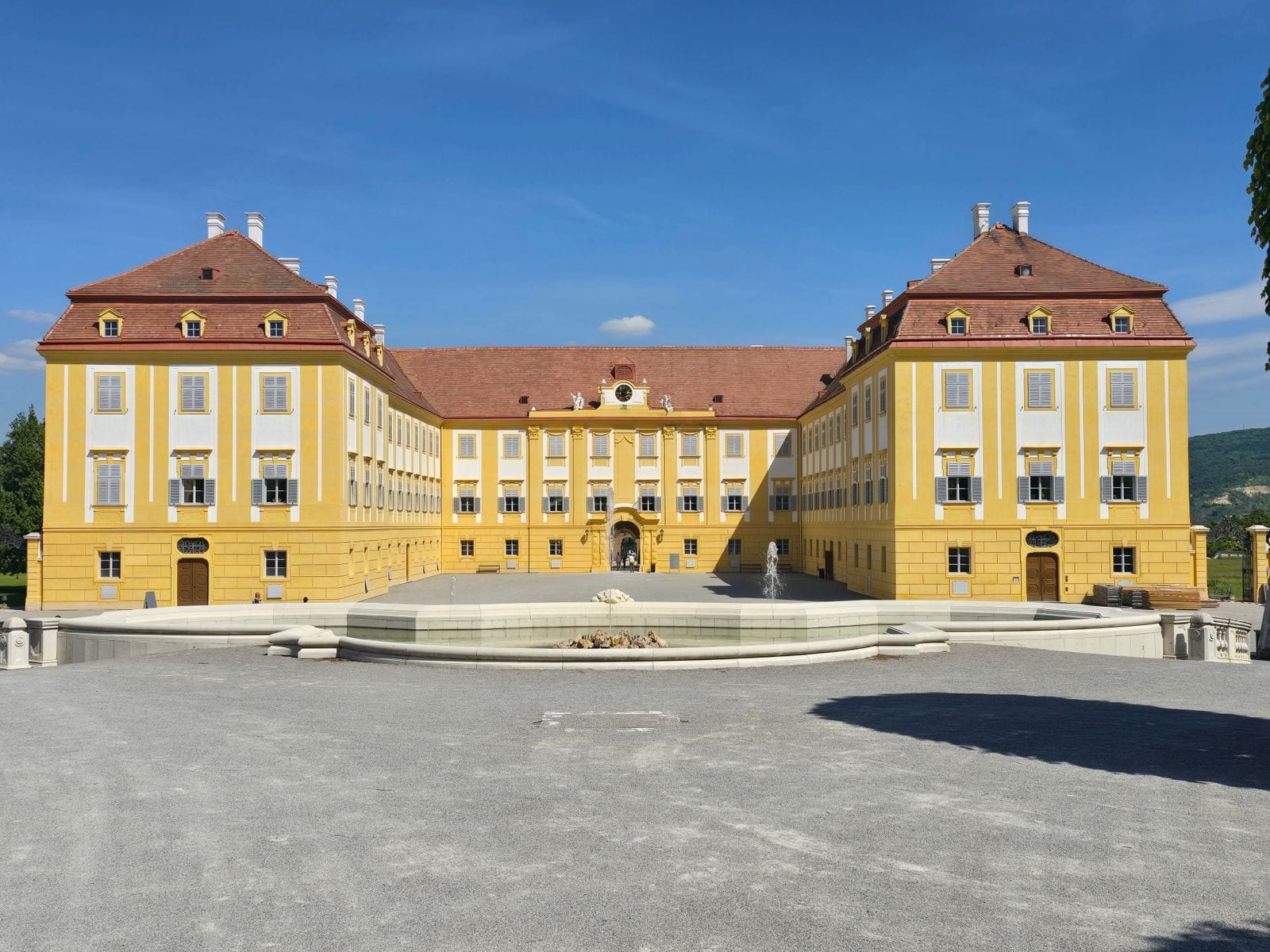Žltý barokový zámok Schloss Hof s čestným nádvorím a fontánou pod modrou oblohou
