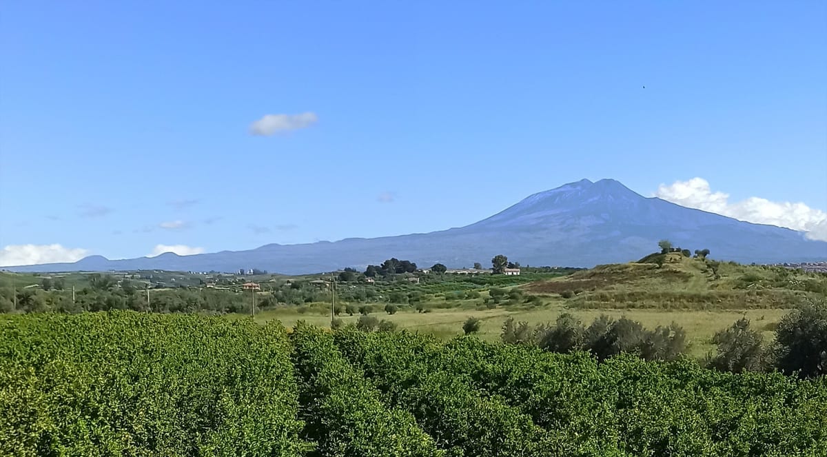 Etna so zasneženým vrcholom nad zelenými sadmi a poľami na Sicílii