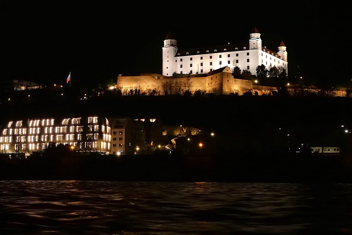 Bratislavský hrad osvetlený v noci nad tmavým Dunajom a svetlami nábrežia