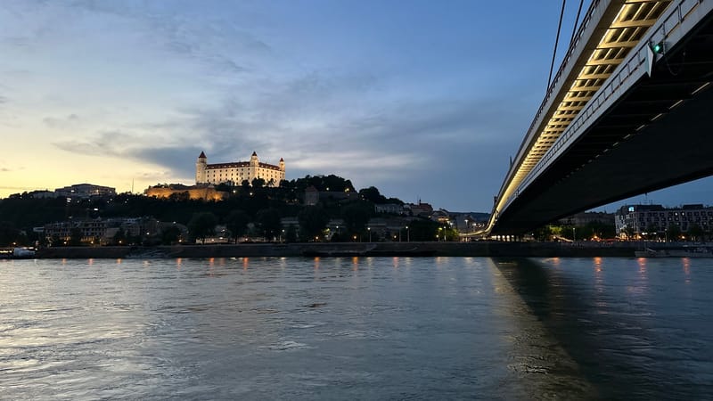 Osvetlený Bratislavský hrad za súmraku nad Dunajom a svetlá Mosta SNP