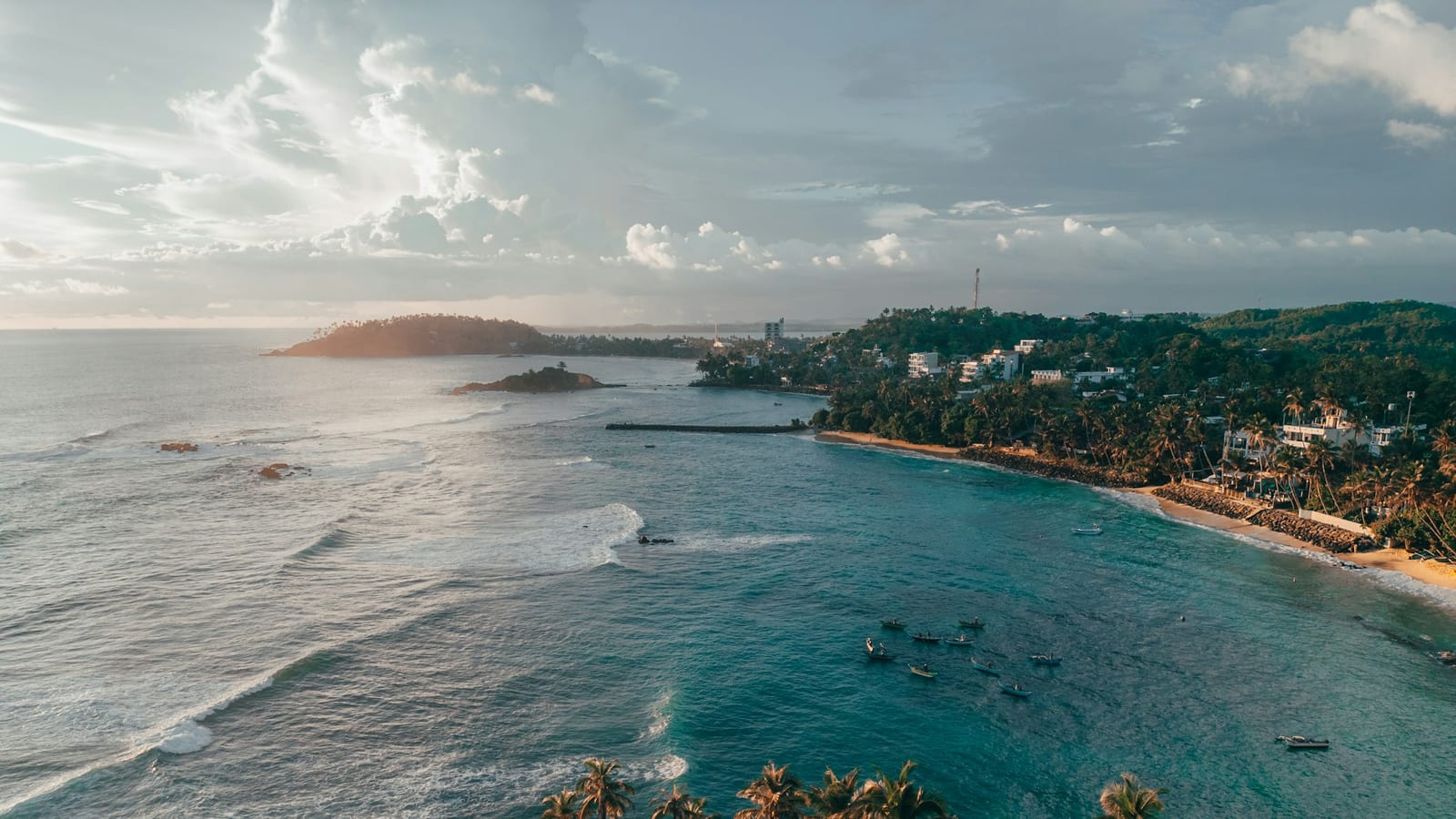 Zátoka a pláž Mirissa na južnom pobreží Srí Lanky z dronu, v popredí palmy na kopci Coconut Tree Hill.