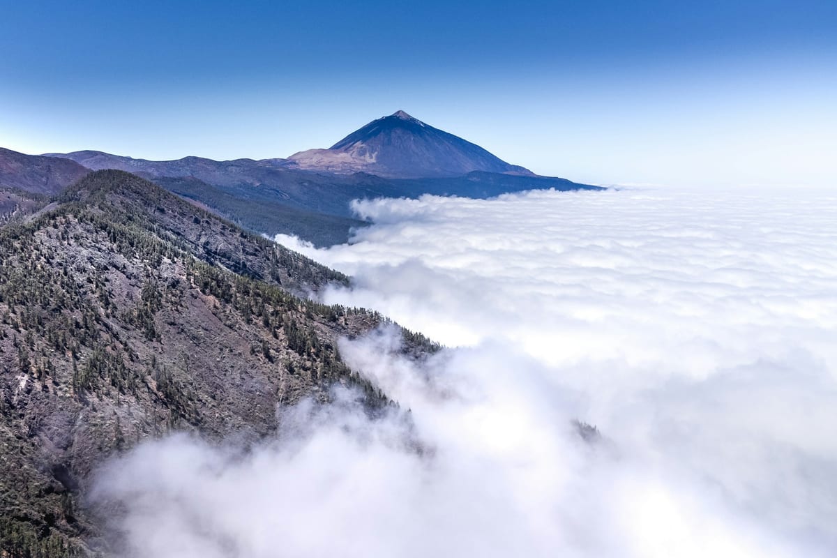 More oblakov pod svahmi Tenerife, nad ním vrchol Teide a modrá obloha