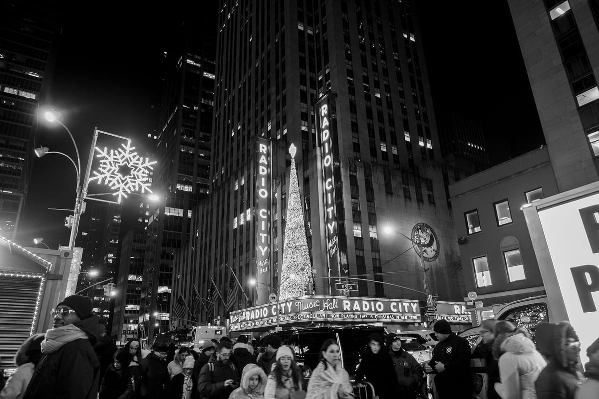 Čiernobiela fotka davu pred osvetleným nápisom Radio City Music Hall v decembri