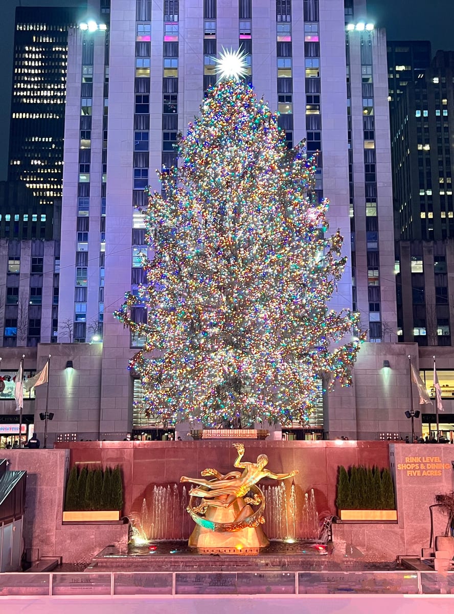 Rozsvietený vianočný stromček v Rockefeller Center večer, pod ním zlatá socha Promethea