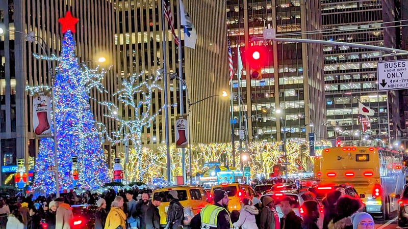 Osvetlený vianočný stromček pred mrakodrapom na Šiestej avenue v New Yorku a dav ľudí v noci